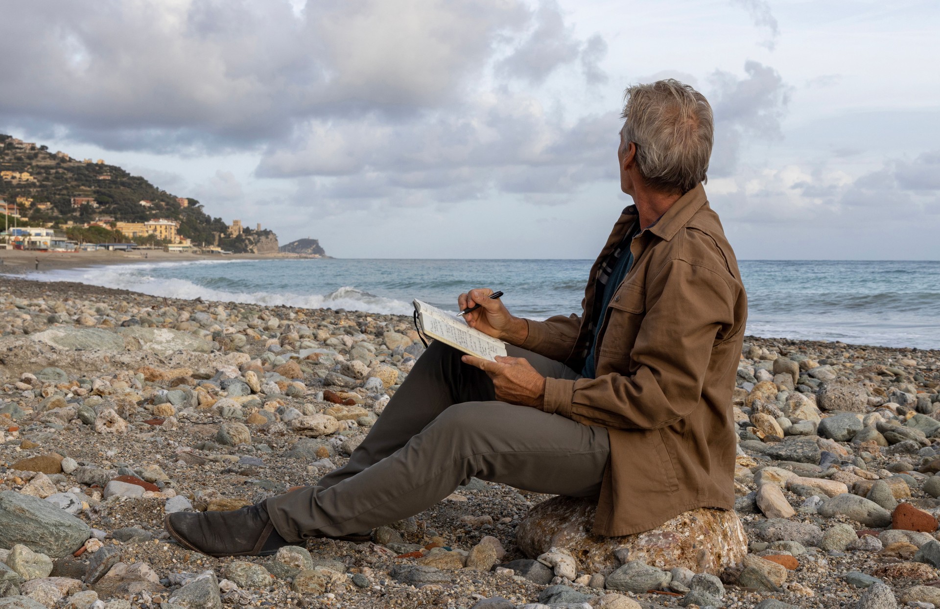 Senior man writes in journal on beach