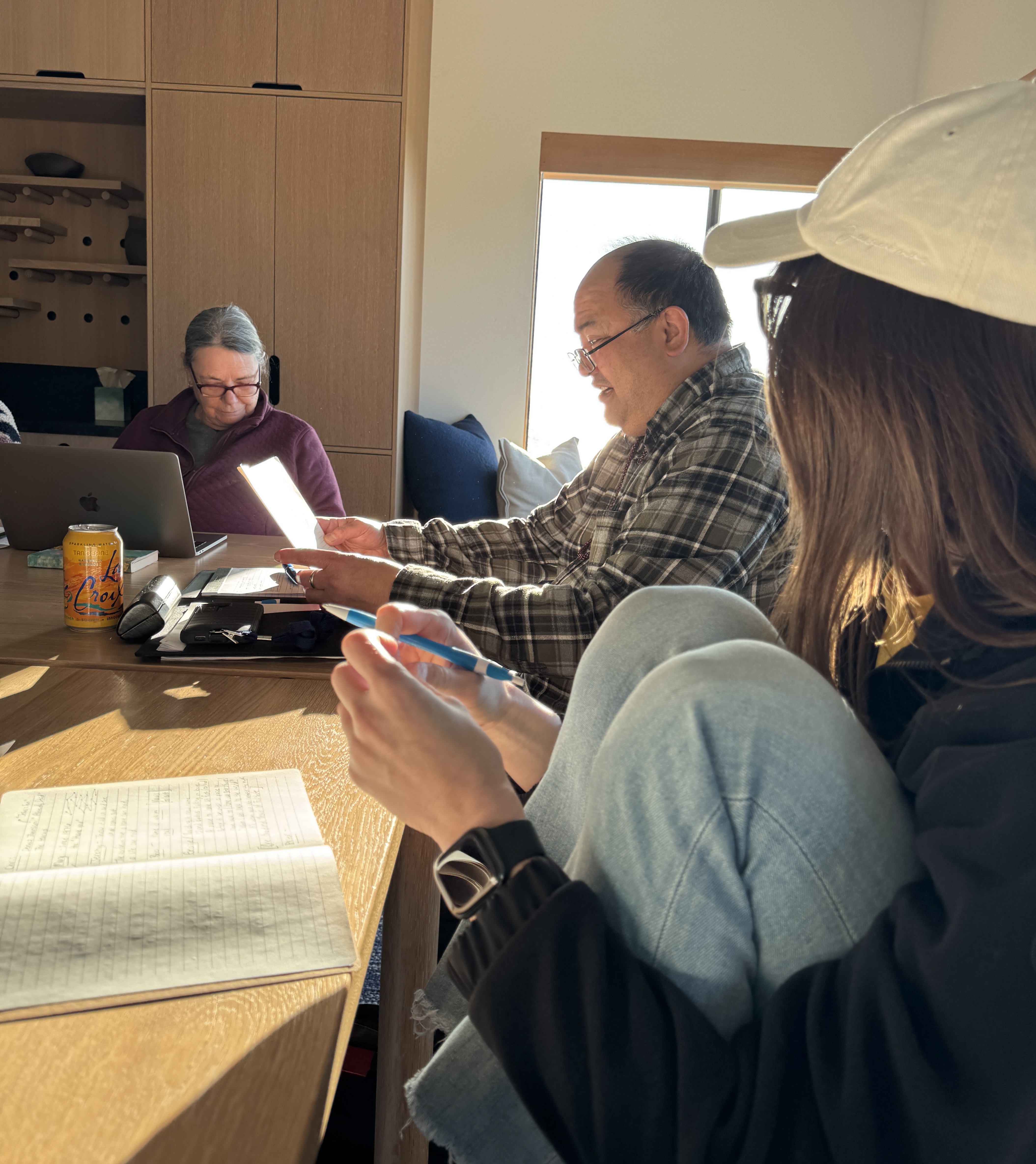 Group writing session — people gathered at a table with notebooks and laptops